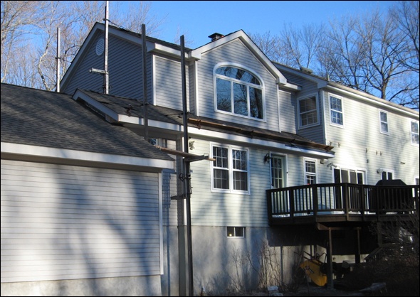 Siding is installed on the back of the house using ladder jacks and scaffolding